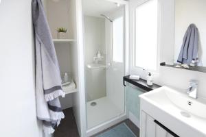 a white bathroom with a shower and a sink at Bungalow Bord de mer in Gouville-sur-Mer