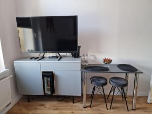 a table with two stools and a television on a white cabinet at Apartamenty Zakonne "Apartament Rycerza" in Malbork