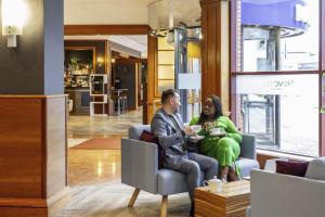 a man and woman sitting in a chair in a lobby at Novotel Bristol Centre in Bristol