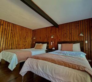 2 camas en una habitación con paredes de madera en Hotel El Tirol en Alto del Roble