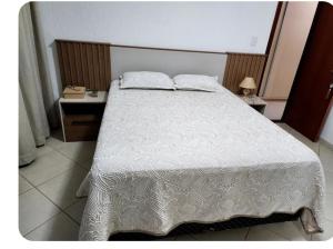 1 dormitorio con 1 cama con edredón blanco en Quarto no Apartamento Neves, en Araxá