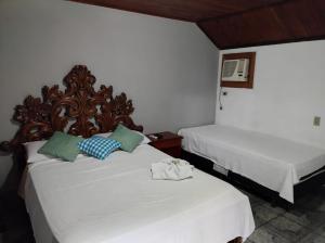 um quarto com 2 camas com lençóis brancos e almofadas verdes em Pousada Nova Conquista em Penedo