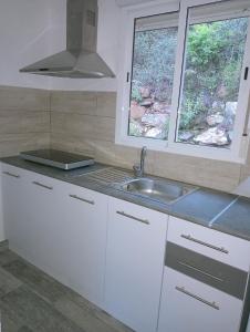 eine Küche mit weißen Schränken, einem Waschbecken und 2 Fenstern in der Unterkunft Rural Sant Llop in Tordera