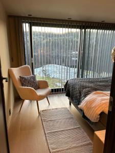 1 dormitorio con cama, silla y ventana grande en Perle ved sjøen! Ny hytte på 90m2. en Kragerø
