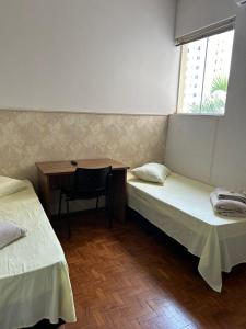 a room with two beds and a desk and a table at CENTRALHE HOTEL in Marília