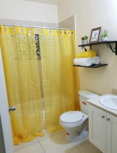 a bathroom with a yellow shower curtain and a toilet at Gems Pool Side Chillax Stay in Portmore