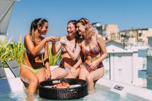 three women in bathing suits sitting on the edge of a swimming pool at Hotel Estense in Gatteo a Mare