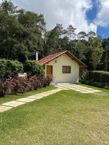 uma pequena casa branca com um jardim de relva em Pousada Brisa da Mantiqueira em Monte Verde