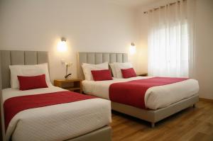 two beds in a hotel room with red and white sheets at Nova Delpa AL in Caldas da Rainha