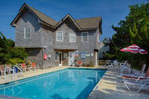 a house with a swimming pool with chairs and an umbrella at The Castle B&B on Silver Lake in Ocracoke