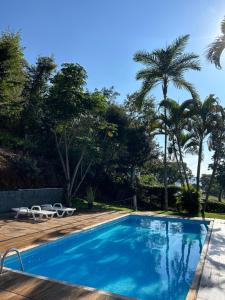 a swimming pool with two chairs and palm trees at Mirante do Lago in Capitólio