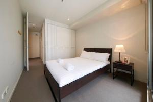 a bedroom with a bed with white sheets and a lamp at Docklands Convenient & Modern 1 Bed Apartment in Melbourne