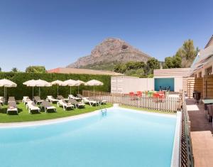 a pool with chairs and umbrellas and a mountain at Hotel Fortuny javea in Jávea