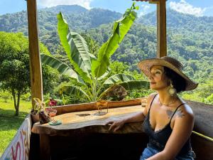 a woman in a hat sitting at a table with a view at Cabaña Guasale (Toucan) in Guachaca
