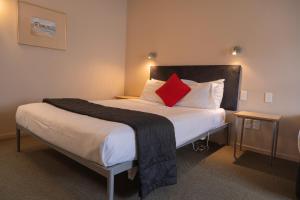 Victoria Court Motor Lodge في ويلينغتون: غرفة نوم بسرير كبير ومخدة حمراء