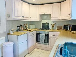 uma cozinha com armários brancos e um forno com placa de fogão em Golf Cottage em Chinley