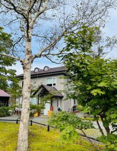 Una casa blanca con un árbol delante. en 民泊JOYFUL天然温泉付きログハウス en Shiraoi