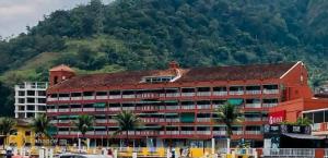 a large red building with palm trees in front of a mountain at Apart Hotel no Piratas Angra dos Reis in Angra dos Reis