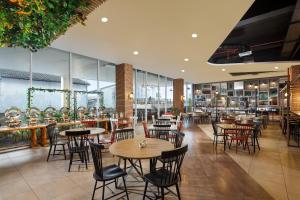 un restaurant avec des tables, des chaises et des fenêtres dans l'établissement Luminor Hotel Purwokerto By WH, à Purwokerto