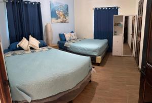 two beds in a room with blue curtains at Casa del Sol, Barra de Santiago in Barra de Santiago