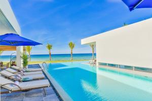 a swimming pool with chairs and an umbrella next to the ocean at Diamond Beach Villa Da Nang in Danang
