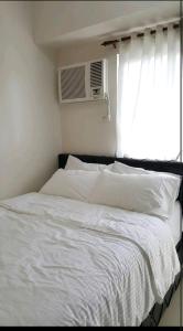 Una cama con sábanas blancas y una ventana con aire acondicionado. en Field Residences Condotel Near Airport, en Manila