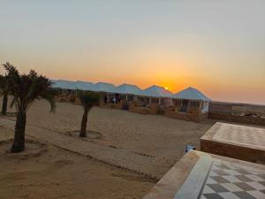 a beach with tents and palm trees and the sunset at THE THAR DESERT CAMP SAM JAISLMER in Sām
