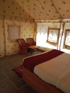 a bedroom with a bed and two chairs in a room at THE THAR DESERT CAMP SAM JAISLMER in Sām