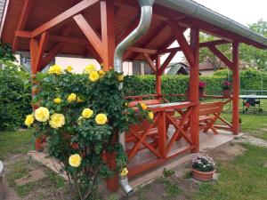 een houten bank onder een prieel met gele bloemen bij Napsugár apartmanház in Balatonlelle