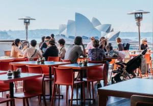 a group of people sitting at tables in front of the opera house at Modern Heritage Home - Stunning Bridge Views in Sydney