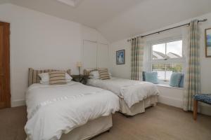 two beds in a white room with a window at Incline Cottage in Portreath