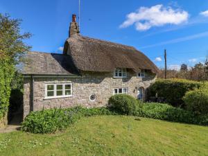 una antigua casa de piedra con techo de paja en Lychgate Cottage en Osmington