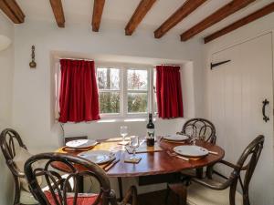 comedor con mesa de madera y cortinas rojas en Lychgate Cottage en Osmington