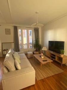 ein Wohnzimmer mit einem weißen Sofa und einem Flachbild-TV in der Unterkunft Profitez de la golden hour depuis Levallois ! in Levallois-Perret