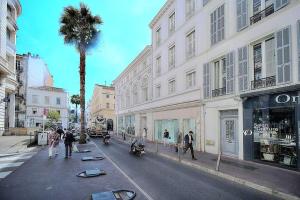 a street with a palm tree and people walking down the street at Palais des festivals et rue d'Antibes charme mansardes in Cannes