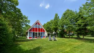 a red and white house with two chairs in the grass at Summio Villapark Schildmeer in Steendam