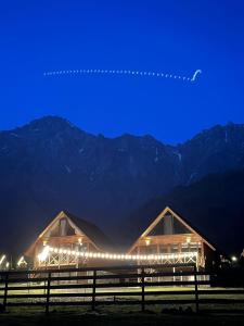 two wooden barns with lights in front of mountains at Cliffside cottage Kazbegi in Stepantsminda