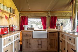 cocina con armarios de madera, lavabo y cortinas rojas en Safari Tent 1 With Log Burning Tub At Tapnell Farm, en Yarmouth