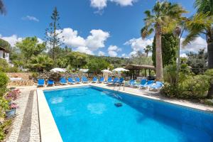 a swimming pool with blue chairs and palm trees at Quinta das Achadas - Jasmine in Lagos