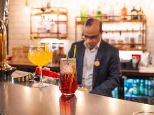 un hombre sentado en un bar con dos bebidas en un mostrador en Novotel Milton Keynes en Milton Keynes