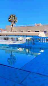 une piscine avec un palmier et un bâtiment dans l'établissement TIRIKA Hôtel La Gazelle, à Zemmour Touirza