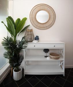 a white console table with a mirror and a plant at OCEANVIEWS BEACH HOUSE / BATEHAVEN in Batehaven