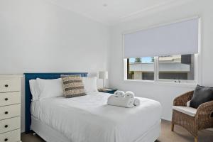 a bedroom with a white bed with a chair and a window at WATERFRONT HOME WITH POOL / SHELLHARBOUR in Shellharbour