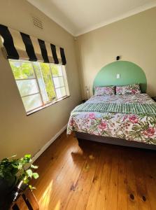 a bedroom with a bed with a green headboard and two windows at Rondebosch Cottage in Cape Town