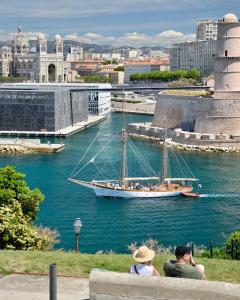 a man and woman sitting on a wall looking at a sail boat in a river at Terrasse - Hyper centre - 2 chambres - Parking gratuit - Calme & lumineux - Arrivée autonome in Marseille