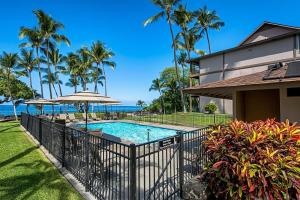 a swimming pool with an umbrella next to a house at Kona Isle A4 in Kailua-Kona