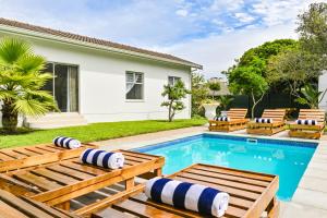 a swimming pool with benches and a house at Spray Lodge in Bloubergstrand
