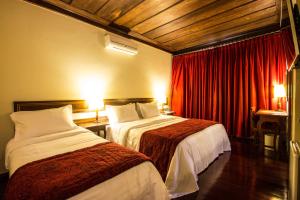 two beds in a hotel room with red curtains at Hotel Pousada do Arcanjo in Ouro Preto