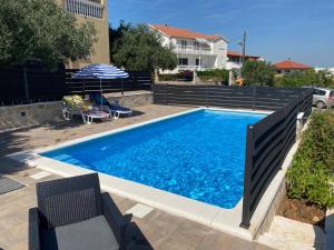 a swimming pool with two chairs and an umbrella at Apartman Telar in Vodice