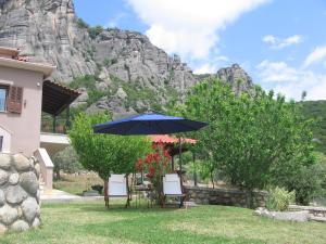 a table and chairs with an umbrella in front of a mountain at Meteora Olio Hills apartment in Kalabaka